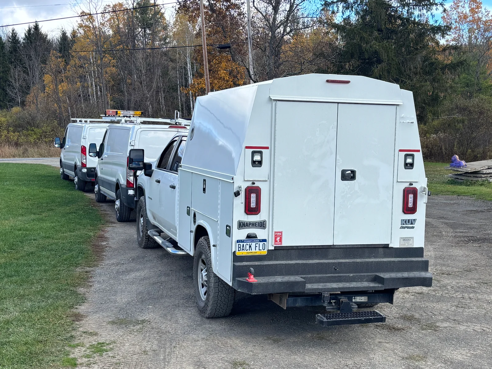 White service vans with storage compartments and roof racks parked in driveway