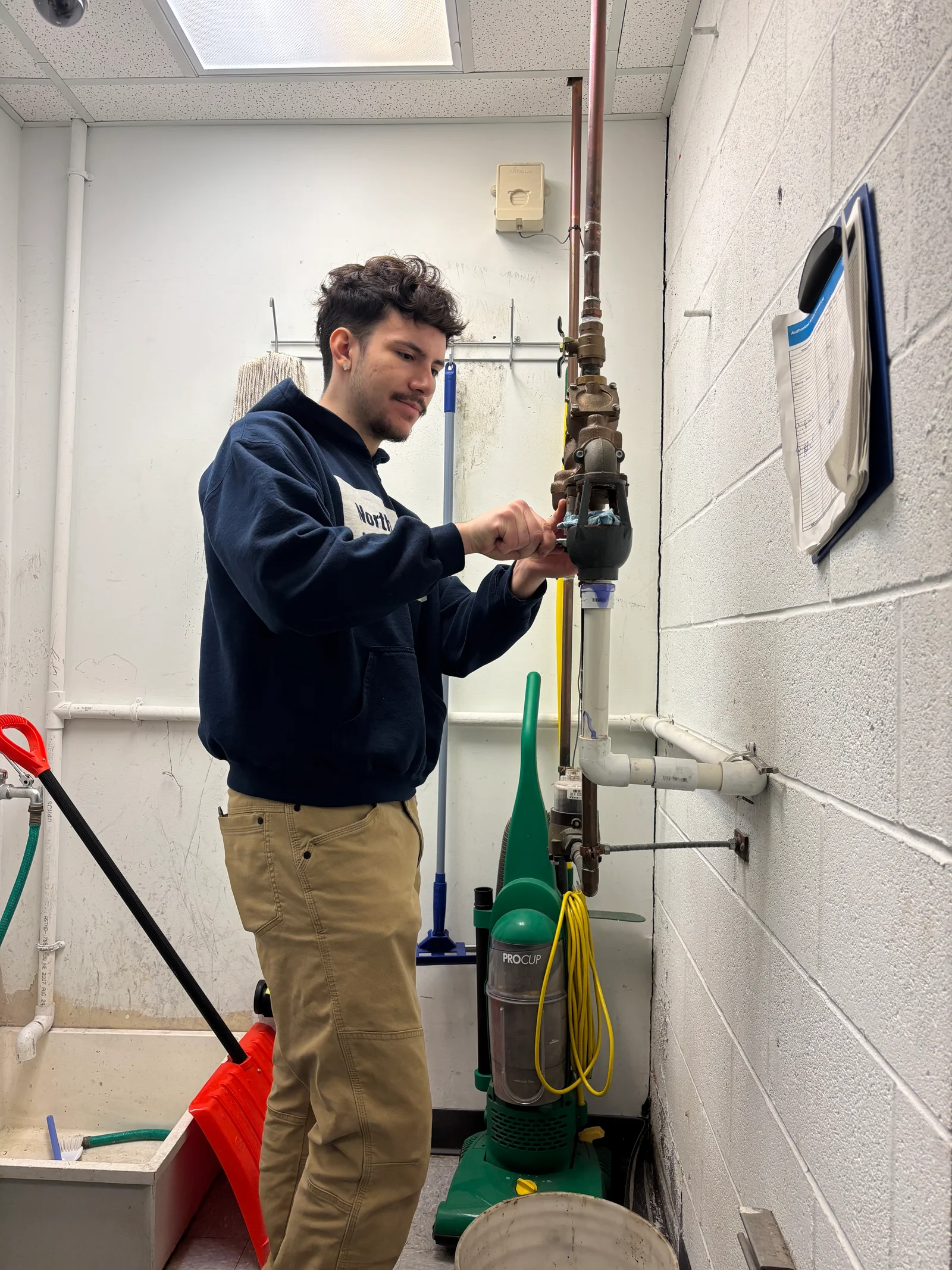 Technician installing backflow preventer valve on vertical copper pipe with green PROCUP device