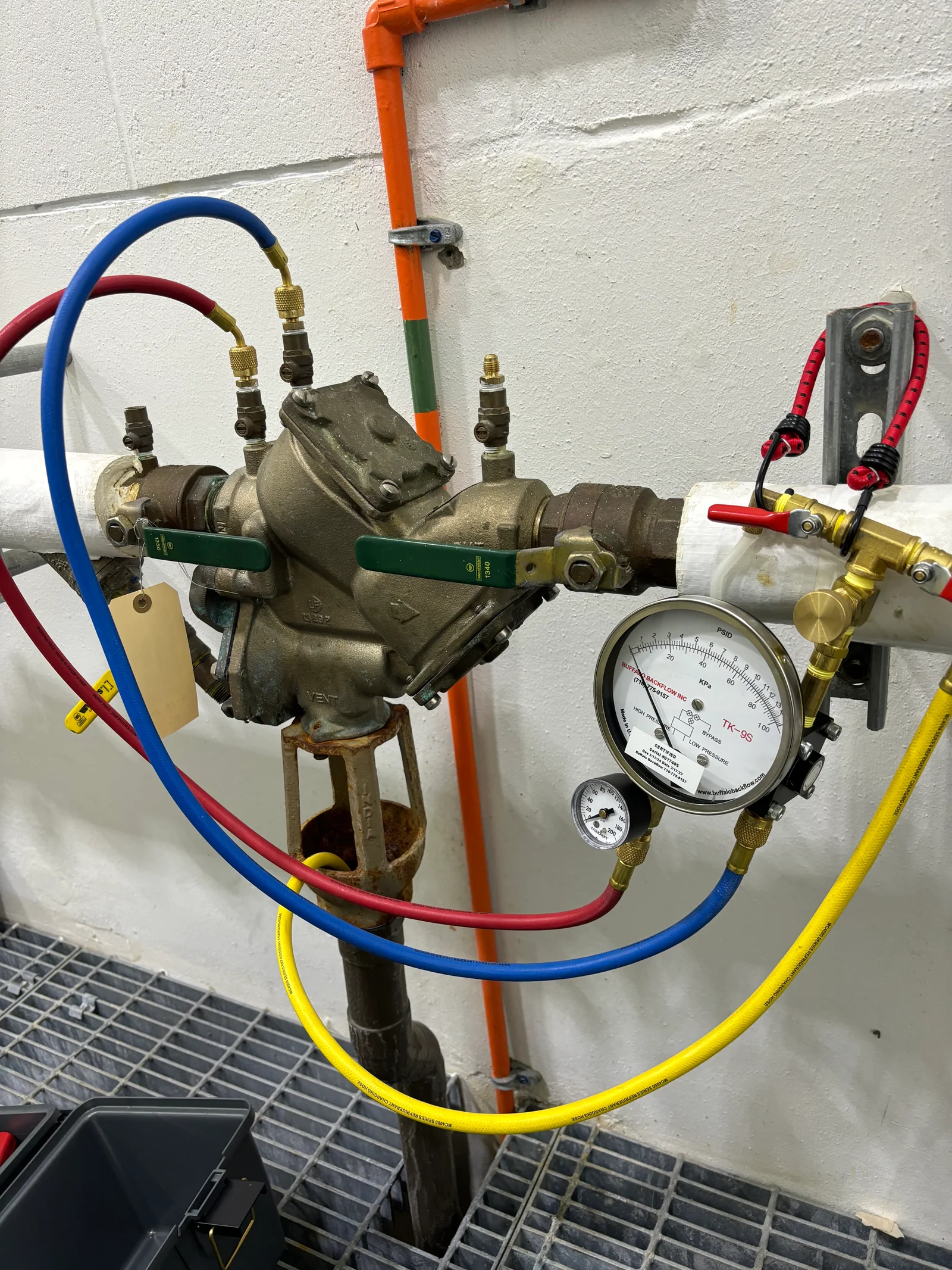 Backflow prevention assembly with dual check valves, pressure gauges, and color-coded test lines on white wall