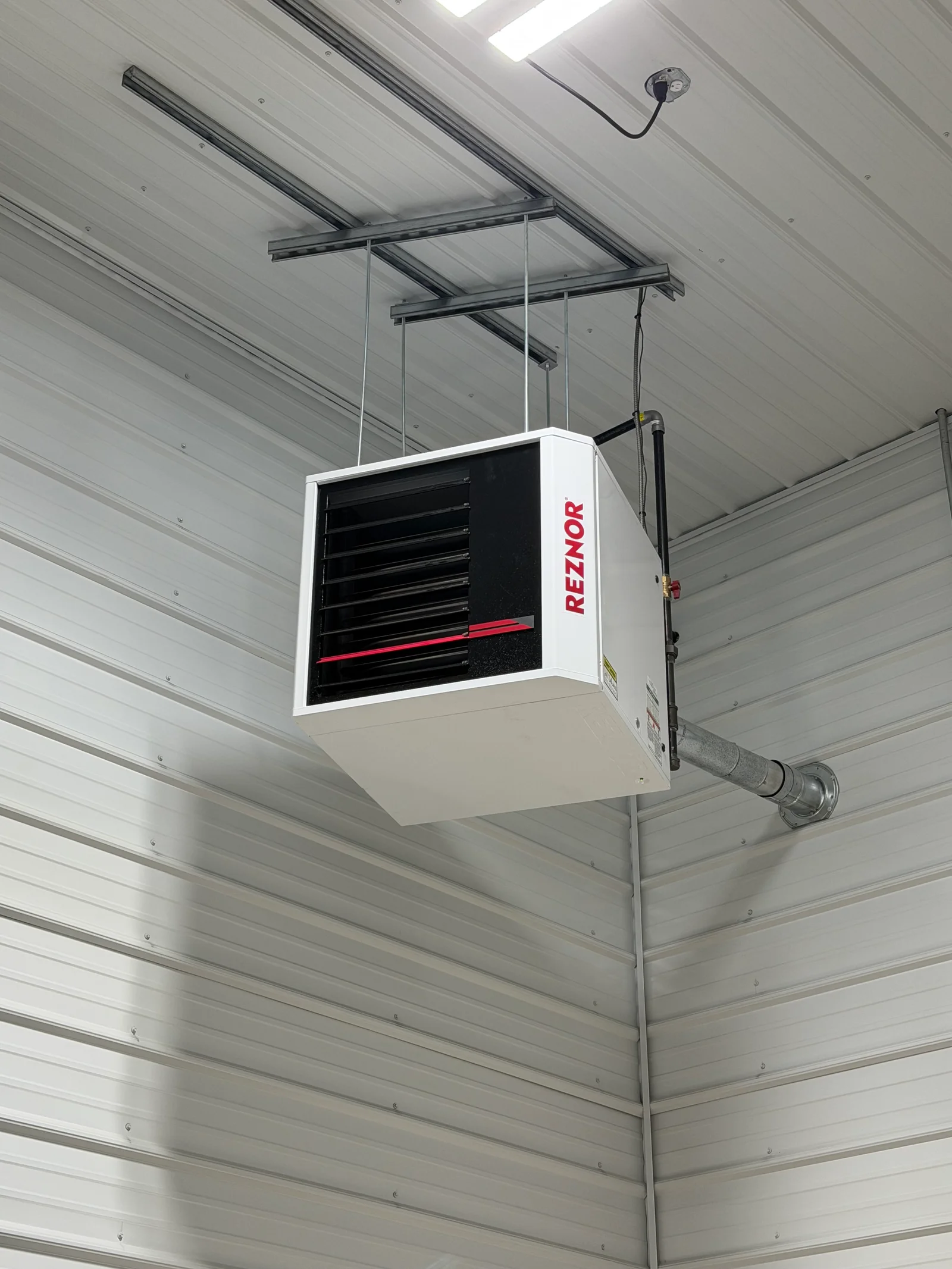 Reznor ceiling heater suspended from steel frame with cable rigging and ductwork in metal building