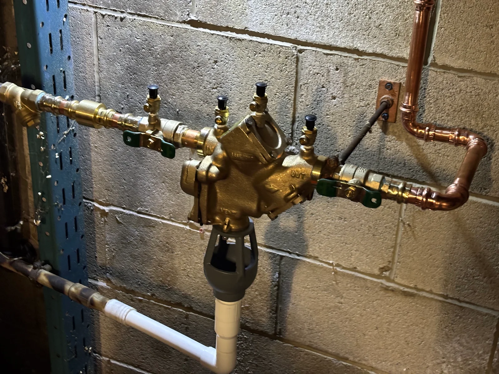 Brass backflow preventer with copper piping, isolation valves, and test cocks mounted on concrete wall