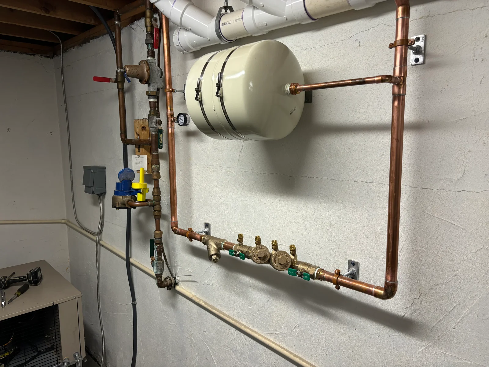 Backflow prevention system with expansion tank, copper piping, and brass valve assembly on basement wall