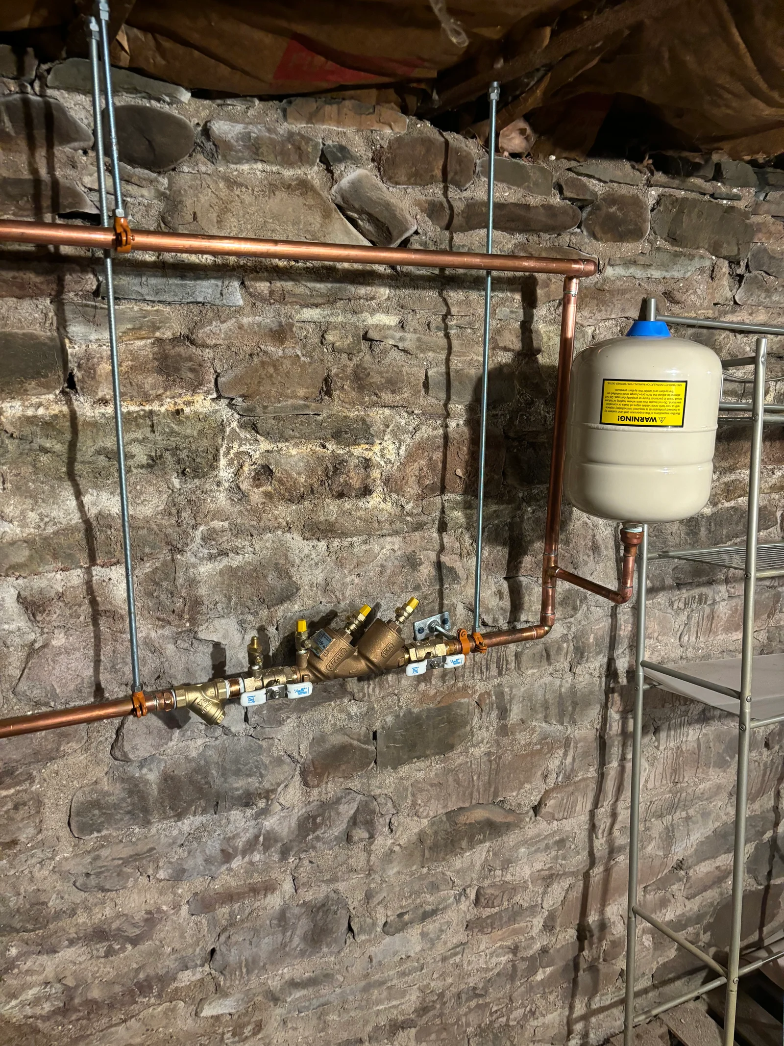 Copper piping with brass backflow prevention valves and expansion tank on stone basement wall