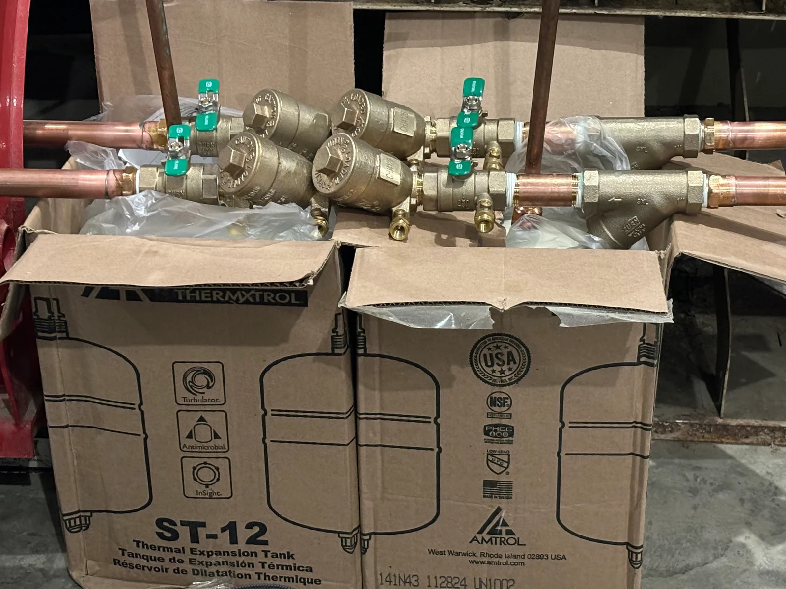 Brass thermal expansion tanks with green ball valves mounted on copper piping with cardboard packaging