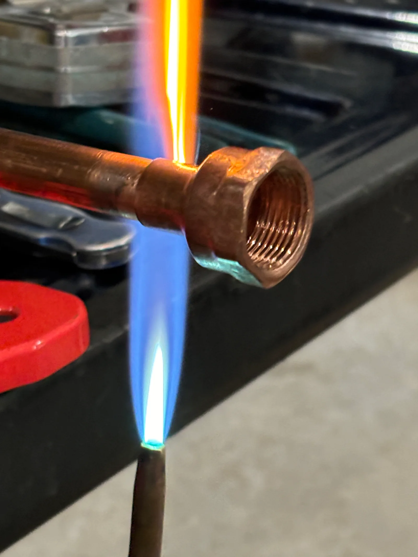 Copper pipe being brazed to brass fitting with oxy-acetylene torch, showing blue flame and solder joint